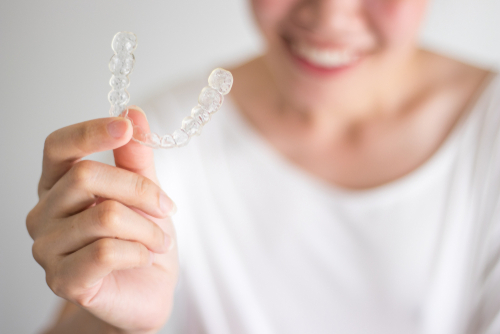 smiling woman holding invisalign or invisible braces, orthodontic equipment-img-blog