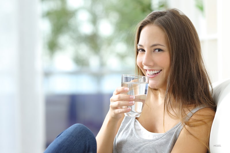 Young woman sipping water while sitting on a couch.