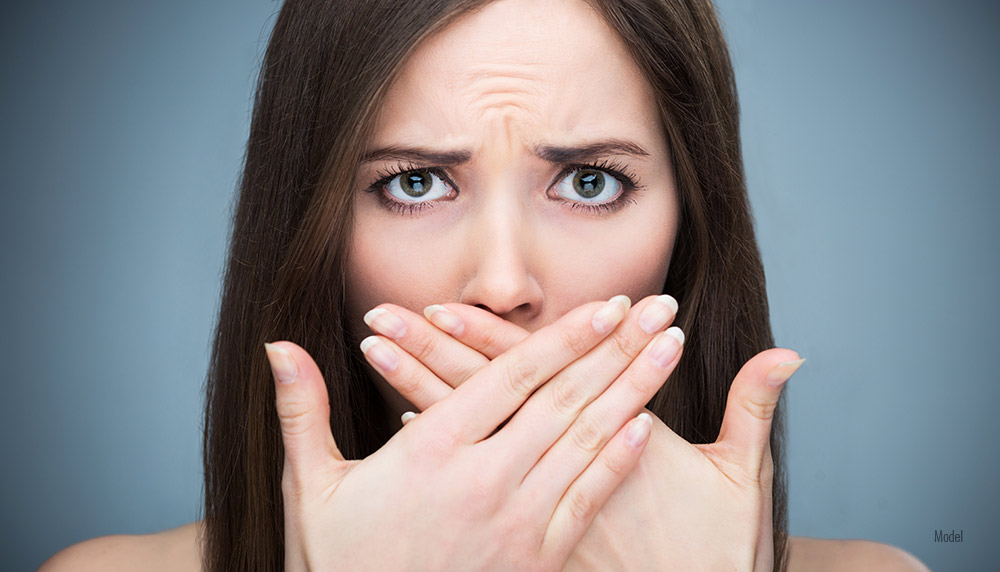 A woman blocks her mouth from her bad breath.